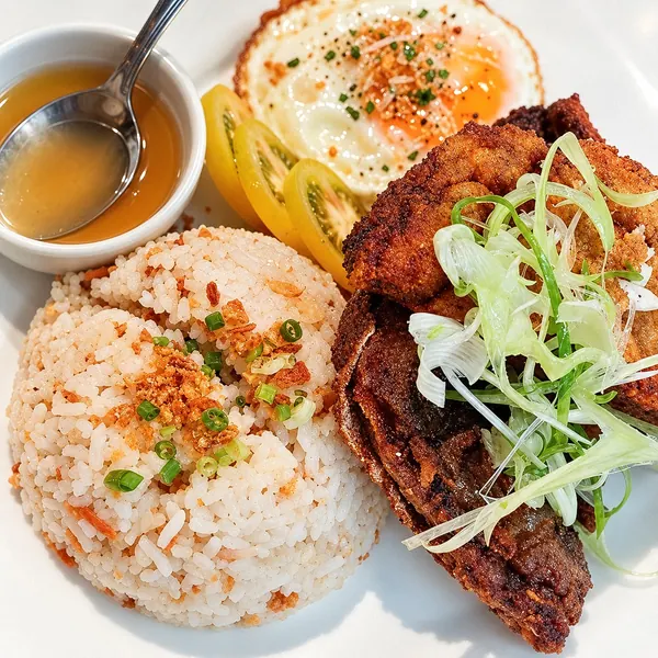 A breakfast plate of garlic rice, a fried egg and crisp fried meat with greens