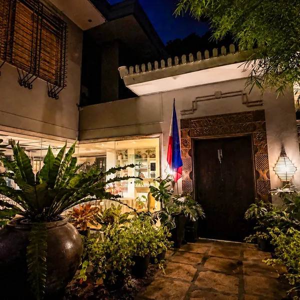 The front of the house at night, lamps glowing among the garden plants by the carved door