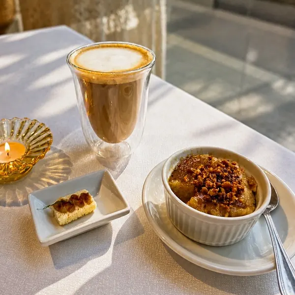 An iced coffee, a slice of cake and a small bowl of dessert on a sunlit table
