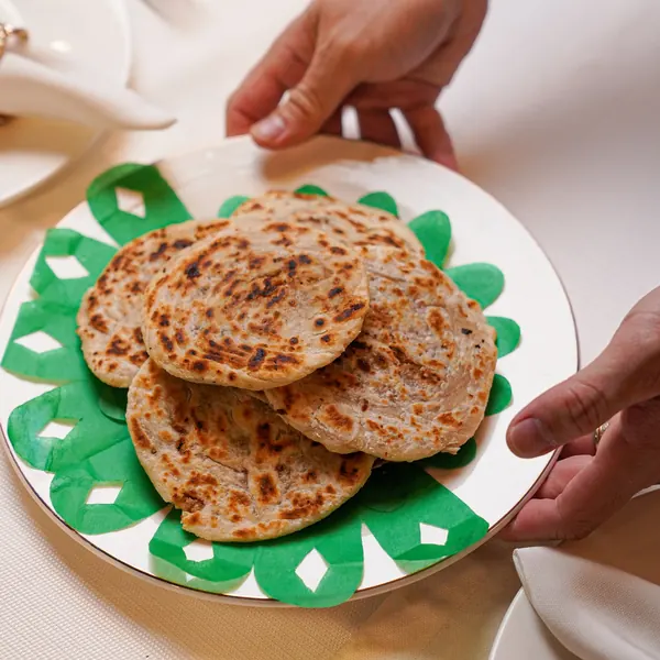 Hands holding a plate of flatbreads on a green patterned plate, part of the Merienda Cena spread