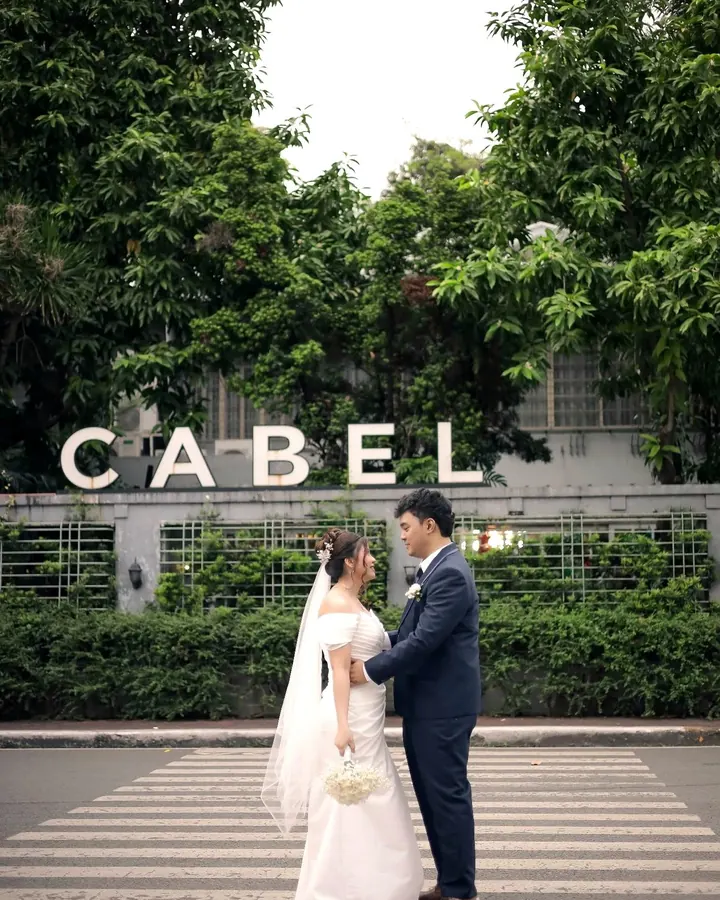 A bride and groom on the street outside the CABEL letters on the front wall