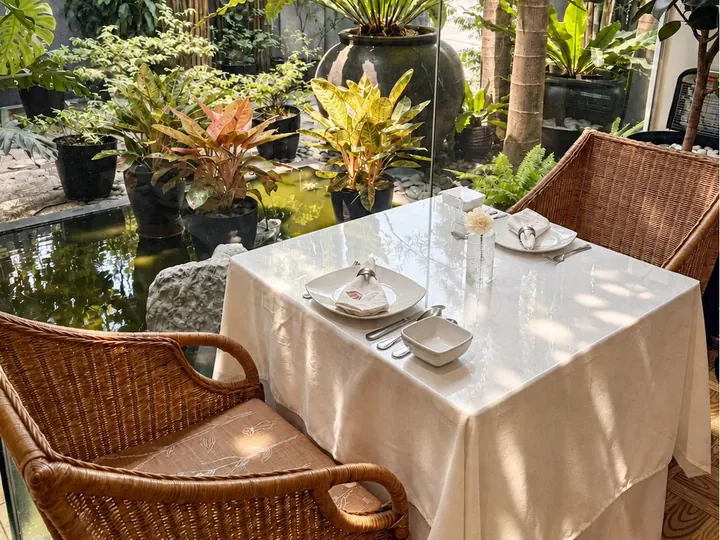 A table set by the koi pond in the garden, with rattan chairs and ferns