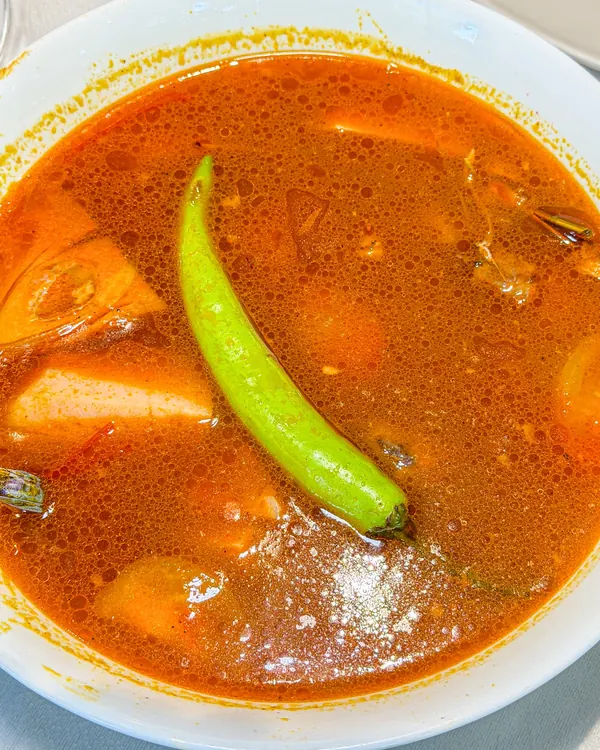 A bowl of kansi, an orange broth with a long green chili