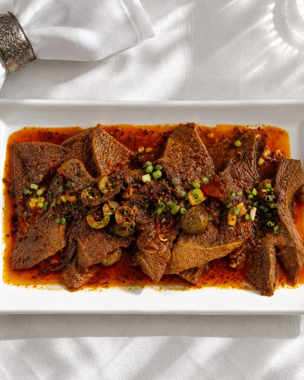 Slices of lengua estofado in a glossy brown sauce
