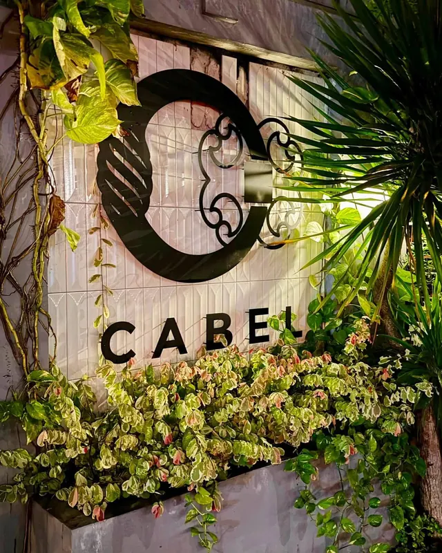 The Cabel C monogram in wrought iron over a wall of trailing plants