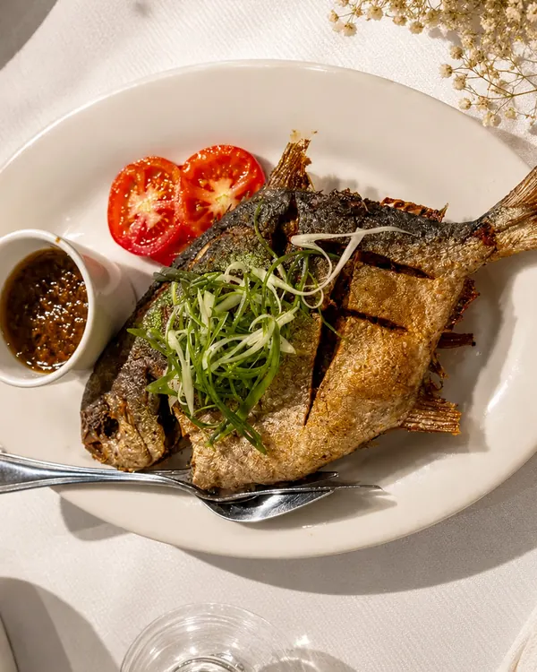 A whole crispy pompano with sliced tomatoes and a small dish of sambal