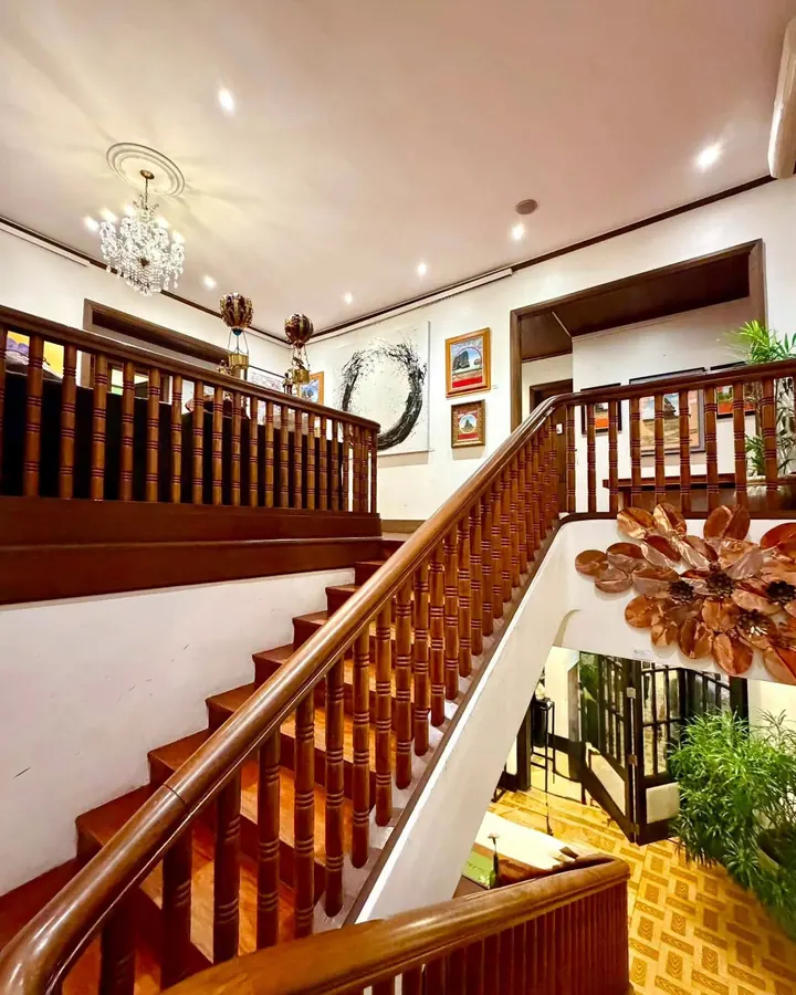 The mansion's wooden staircase and landing, with a chandelier and framed art on white walls