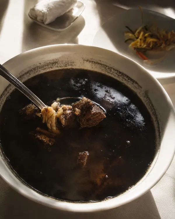 A bowl of tiyula itum, a jet-black broth with pieces of meat