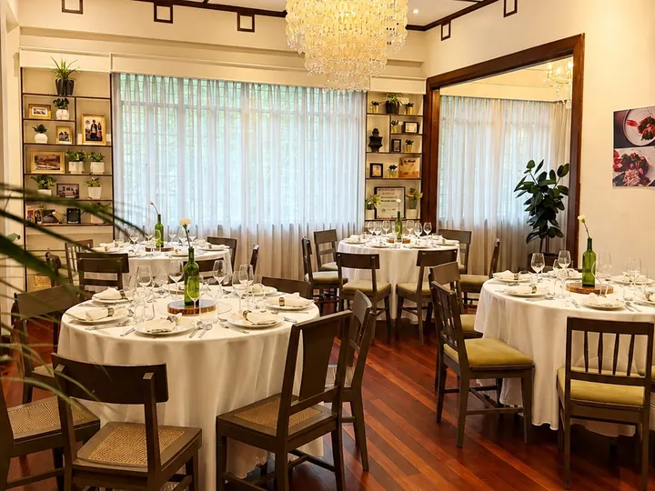 An upstairs dining hall with round tables in white linen, a crystal chandelier and dark wood floors
